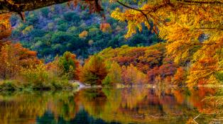 red, yellow, orange and green foliage reflects Texas fall colors over small lake.