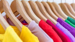 A row of colorful shirts rest on several wooden hangers.  